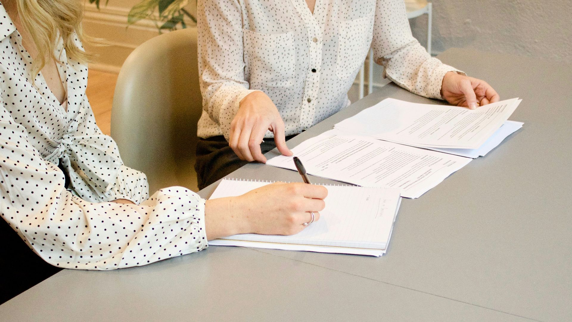 woman signing on white printer paper beside woman about to touch the documents