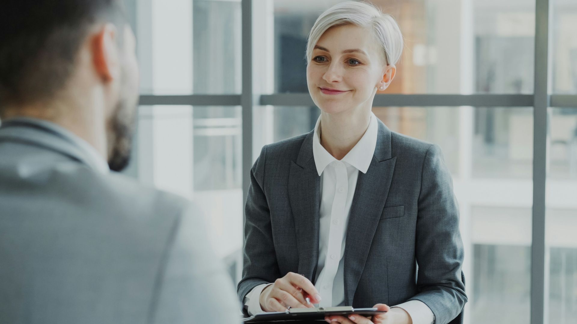 Woman in suit interviews man across table.