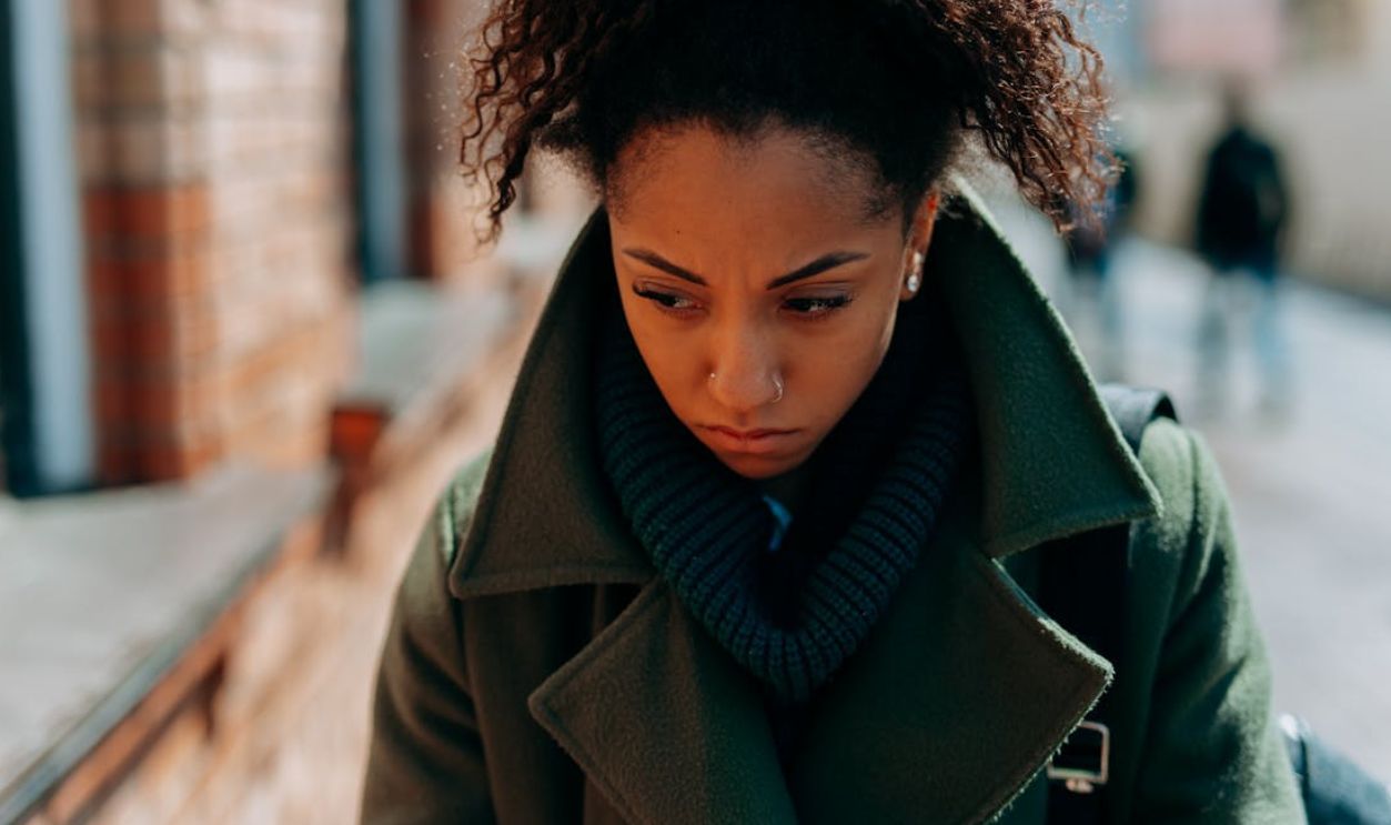 A young woman in a trench coat appears thoughtful and pensive walking down a city street