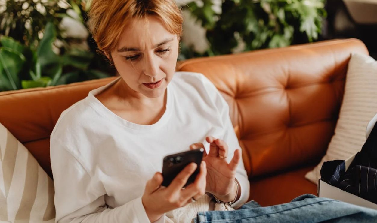 Woman in casual attire using a smartphone on a cozy sofa surrounded by plants