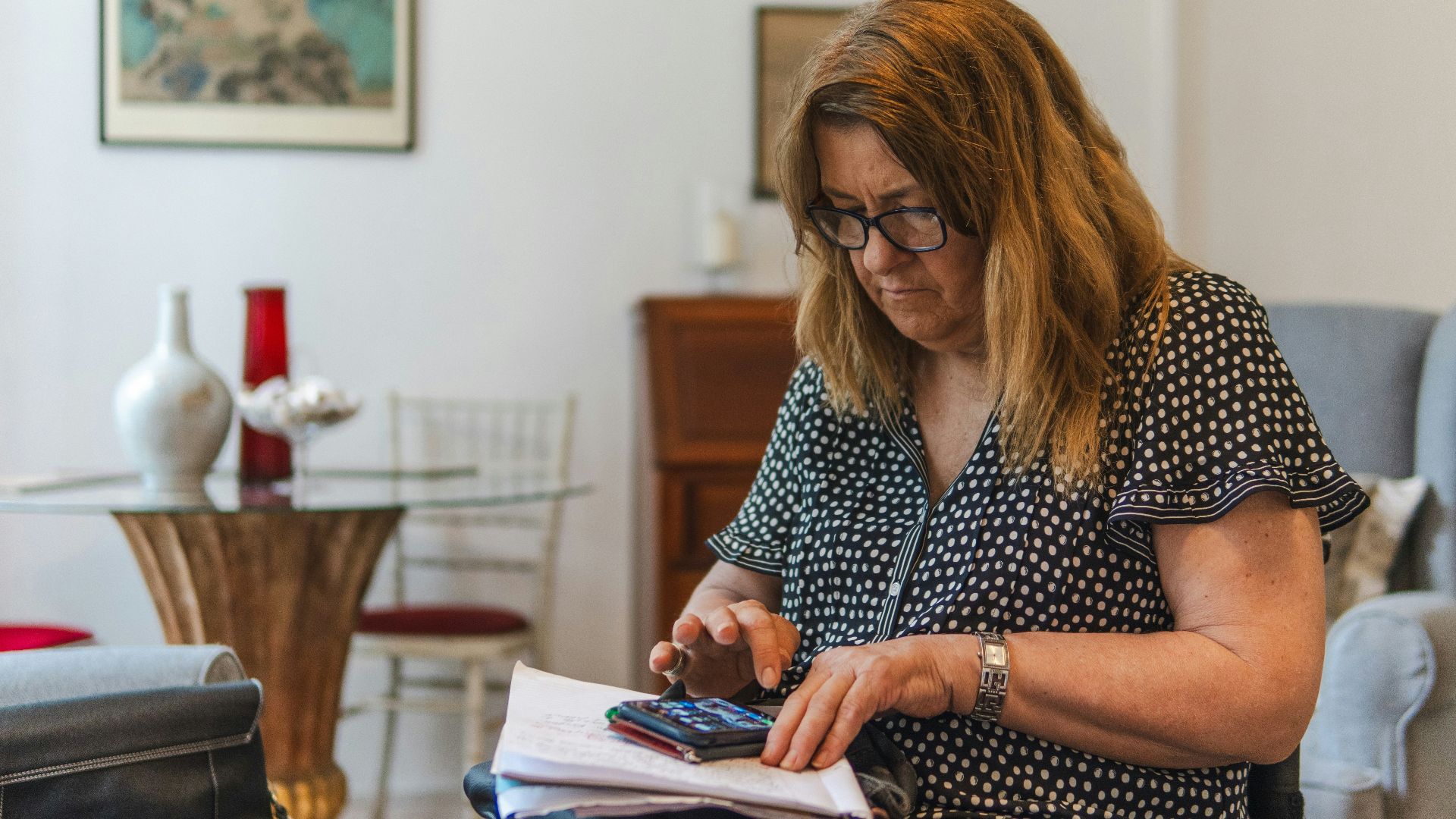 Woman using calculator with papers on table.