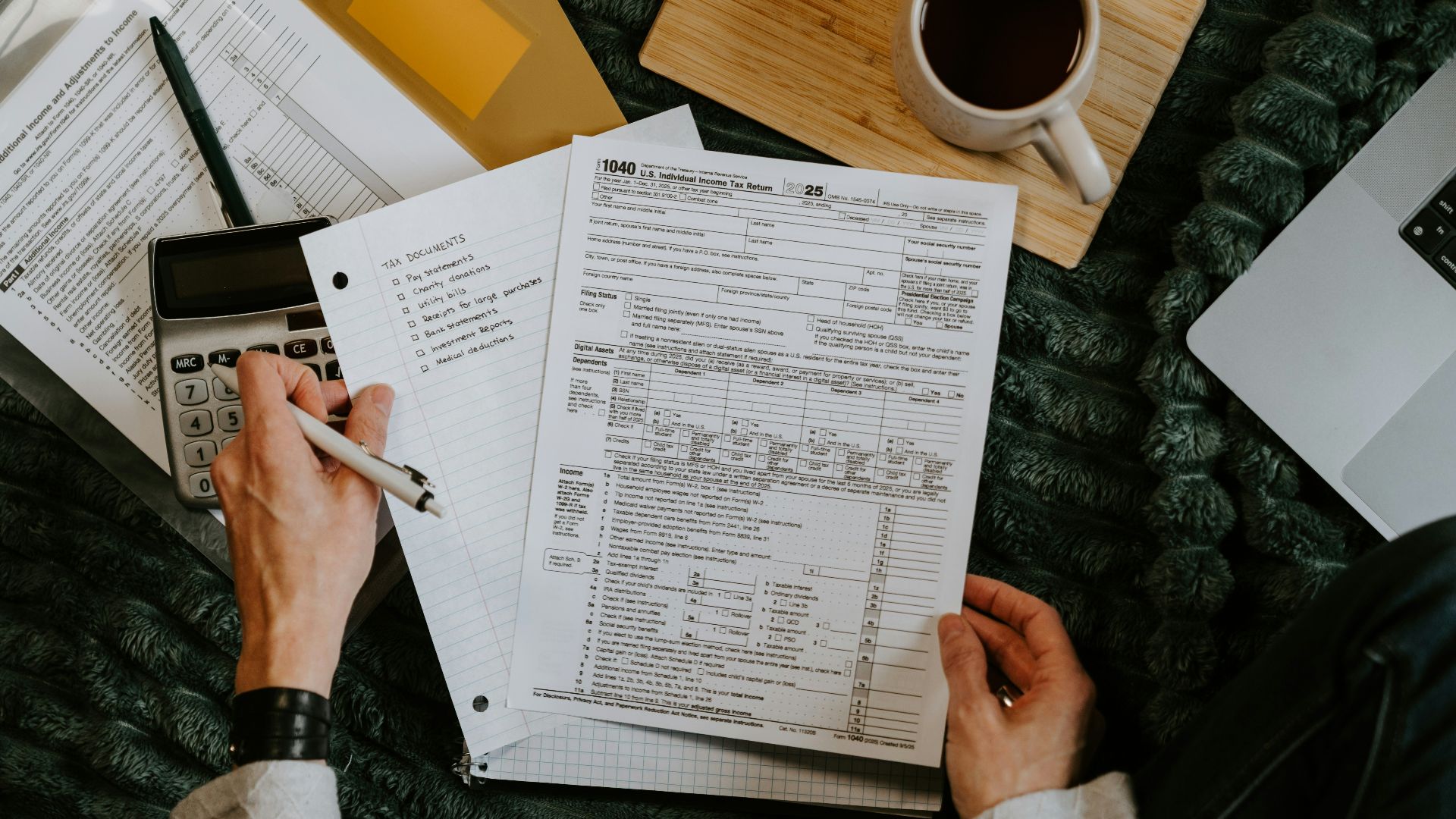 Person reviewing documents with calculator and laptop.
