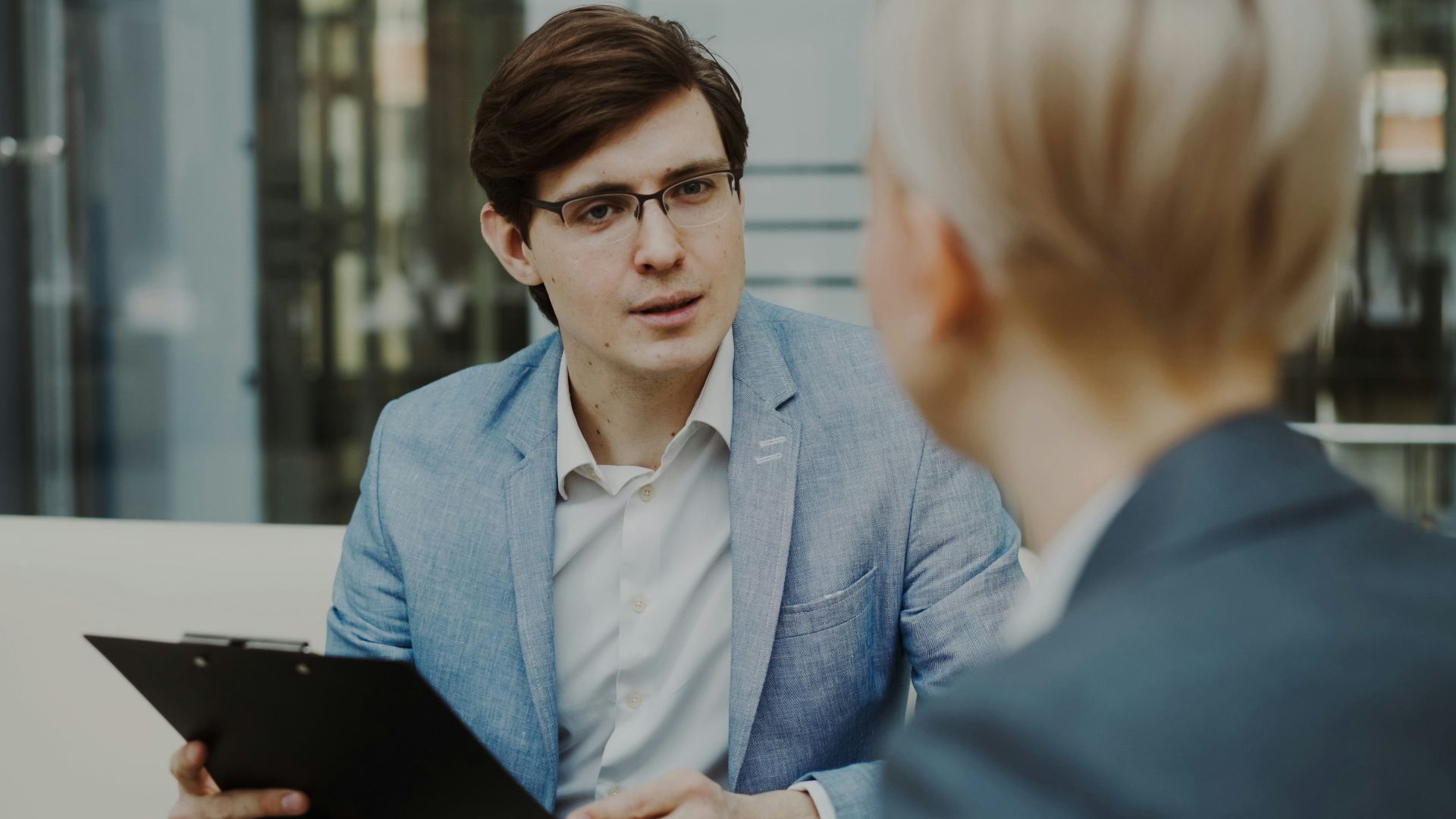 Man in suit holding clipboard talking to woman