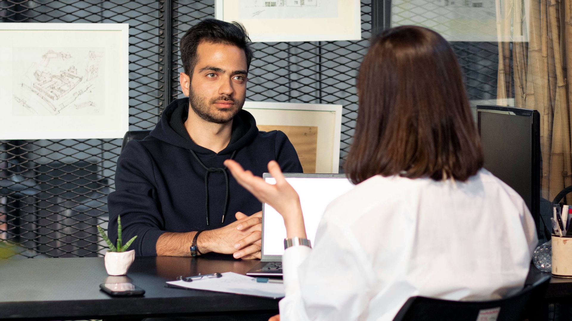 a man sitting at a desk talking to a woman