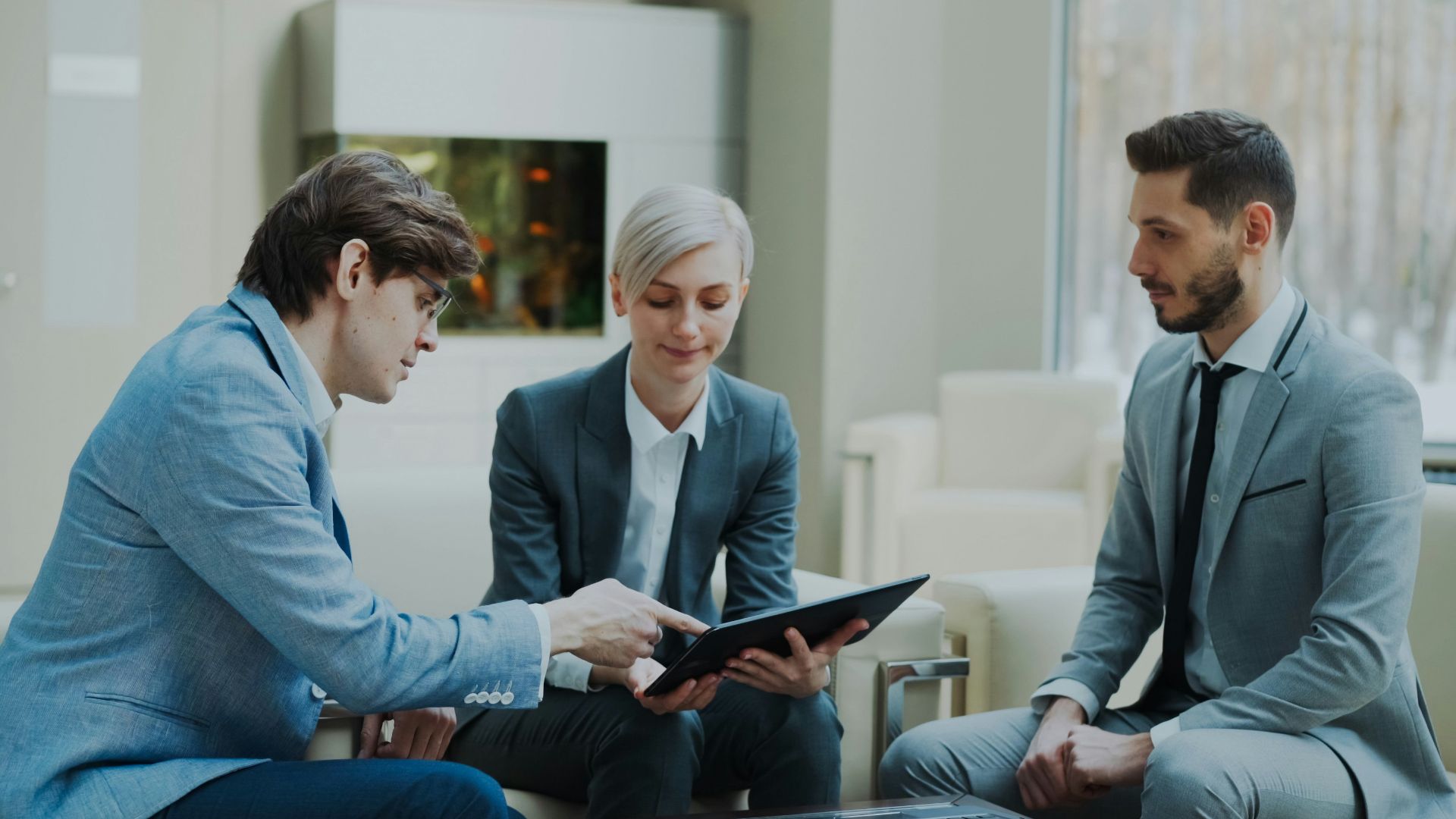 Three professionals discussing a tablet in a modern office.