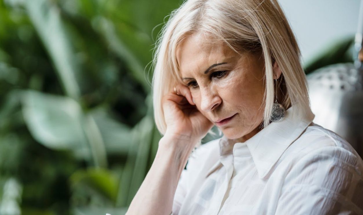 Senior woman in thoughtful pose surrounded by greenery indoors