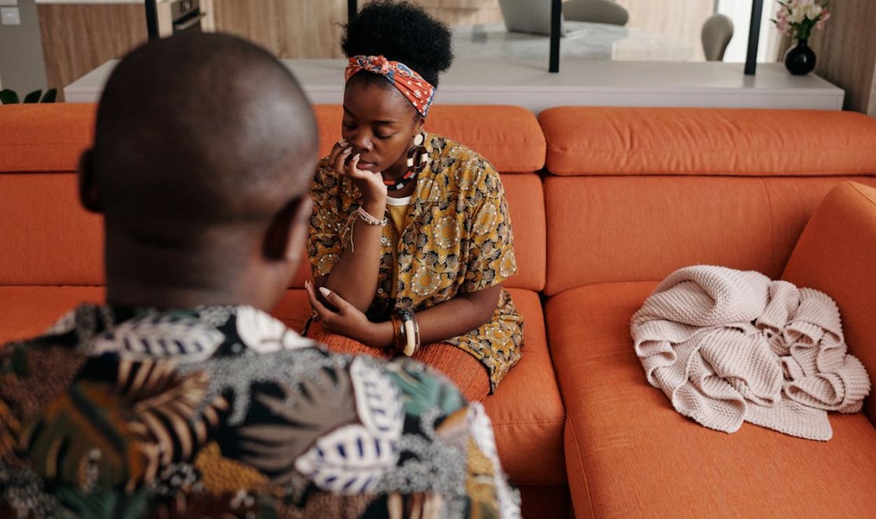 A thoughtful couple engaged in a deep discussion on a vibrant orange sofa in a modern living room.