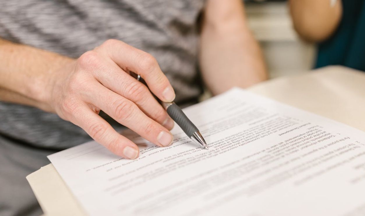 Close-up of a person's hand signing an important legal document with a pen indoors