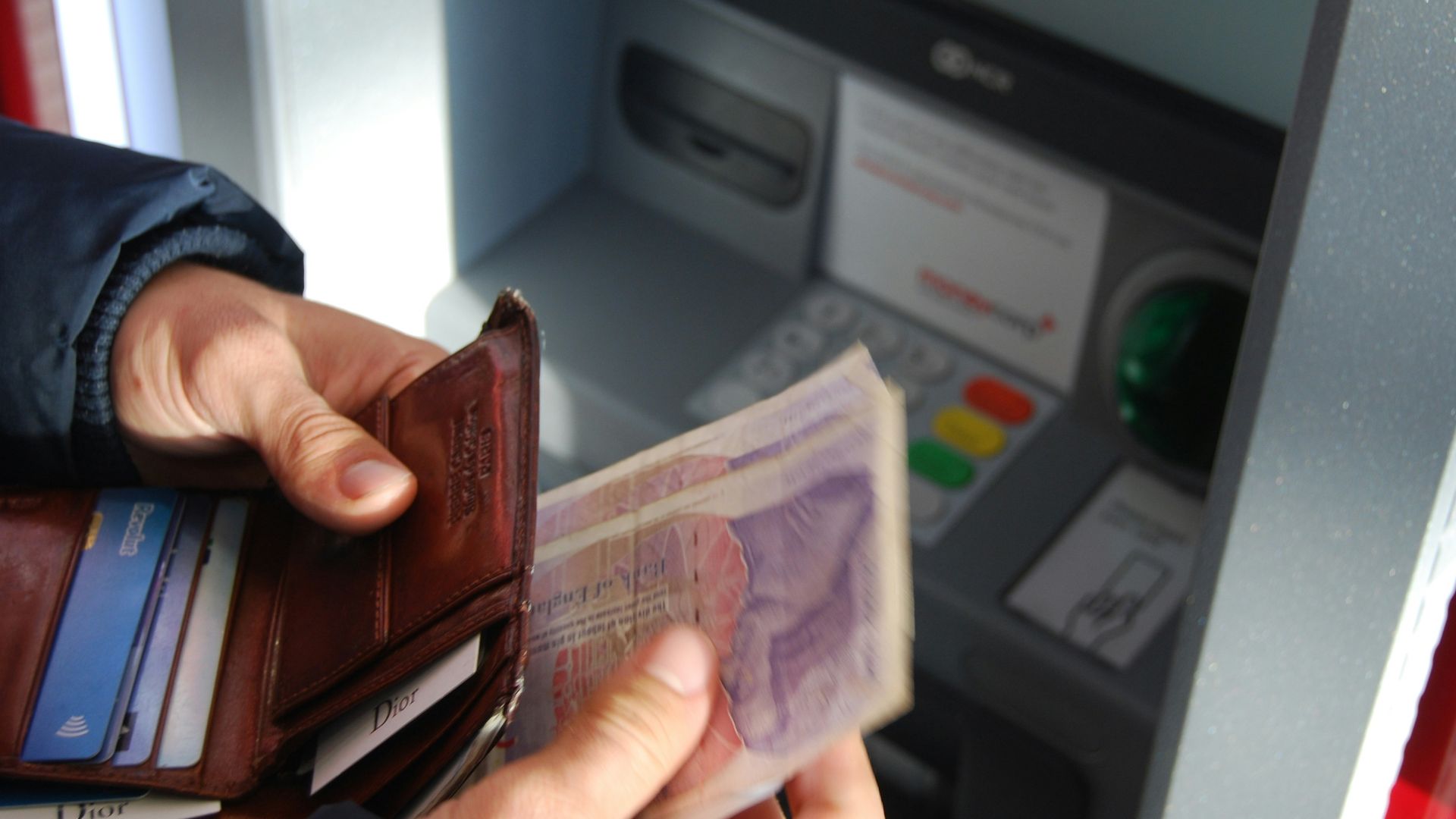 person holding brown leather wallet and banknotes