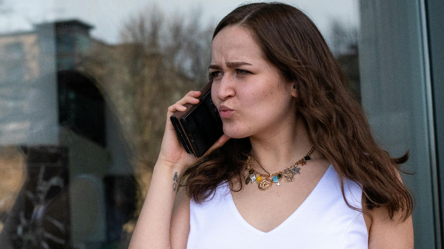 Woman expressing frustration during a phone call while standing outside in daylight.
