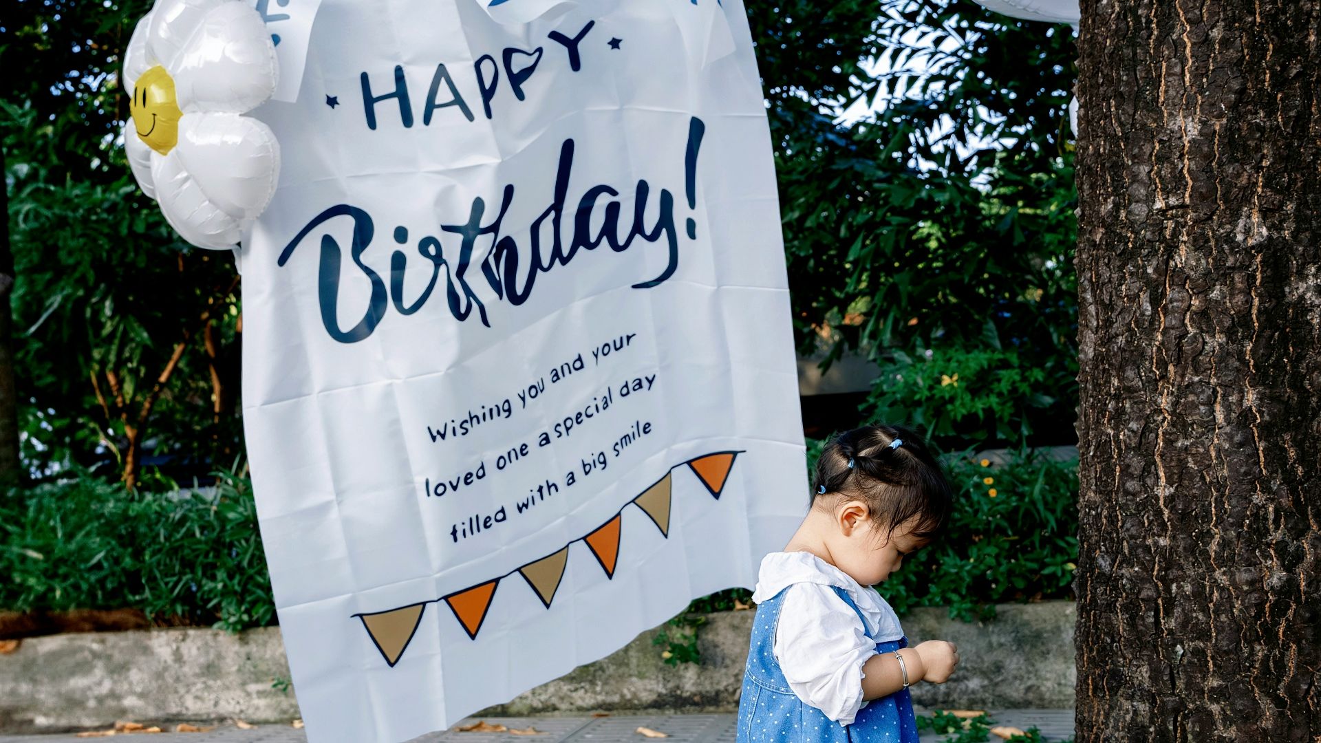 Girl in blue dress near birthday banner with balloons