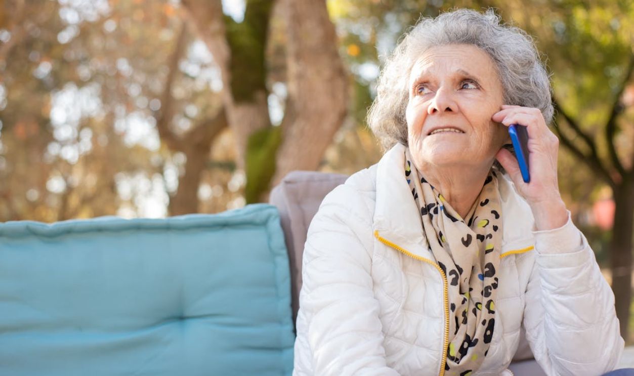 Senior woman in white jacket having a phone conversation in an outdoor park setting