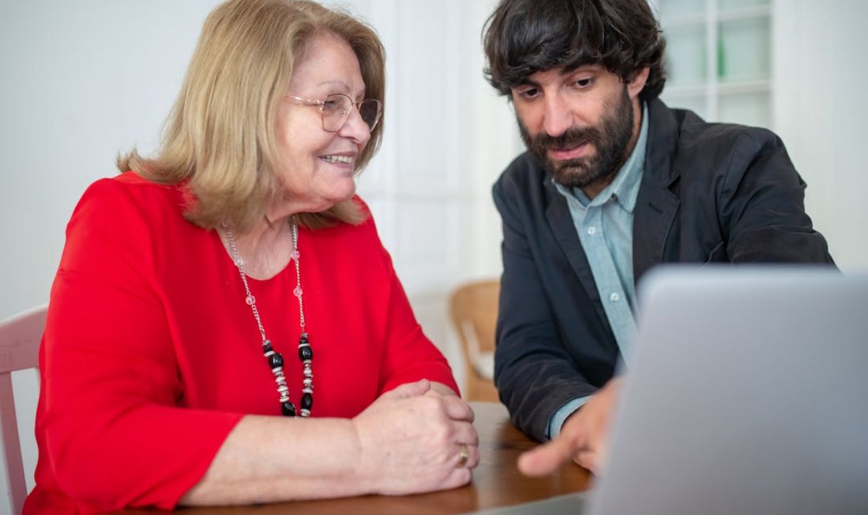 A man and senior woman discuss work on a laptop indoors, focusing on technology and consulting