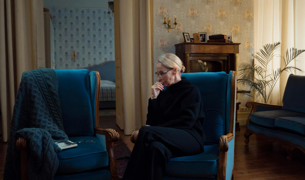 Elderly woman sitting pensively in a cozy living room with vintage decor