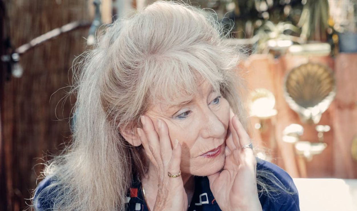 Thoughtful senior woman sitting outdoors, hands on face. A reflective moment captured in sunlight