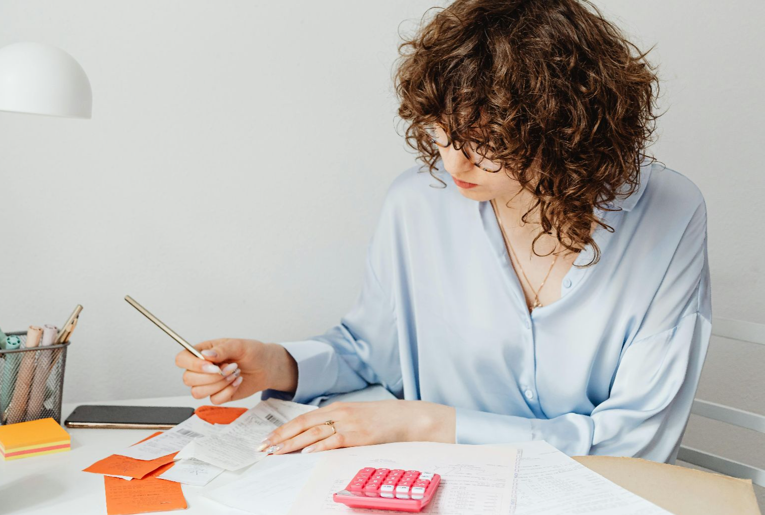 Woman in office calculating expenses with documents, calculator, and coffee.
