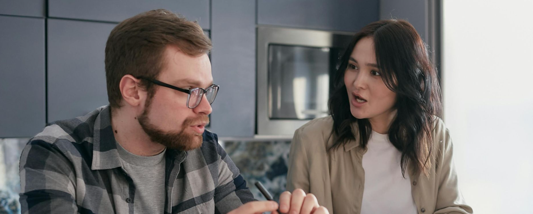 A couple managing finances with gadgets, documents, and coffee mugs at home.