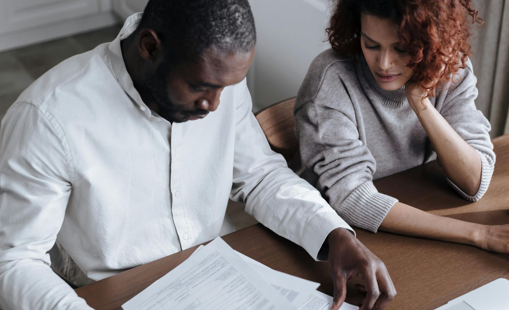 A couple reviews important documents together at a home desk with a laptop.