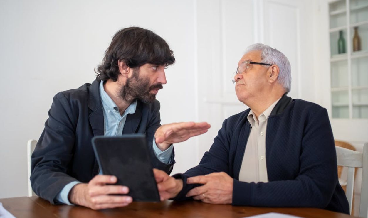 Two men having a professional discussion with a digital tablet at a wooden table indoors.
