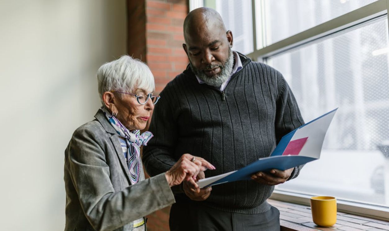 Senior colleagues working together, reviewing documents near an office window.
