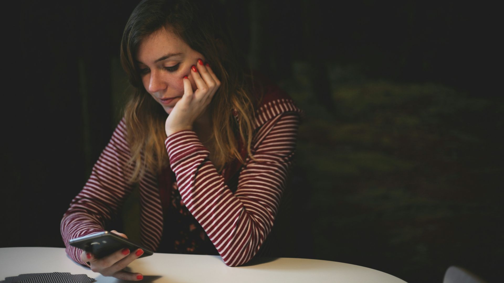 woman leaning on white wooden table while holding black Android smartphone