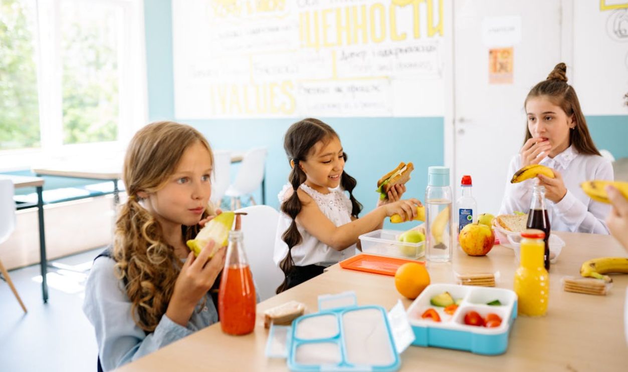 Group of schoolgirls having a break, eating healthy snacks at a canteen table.