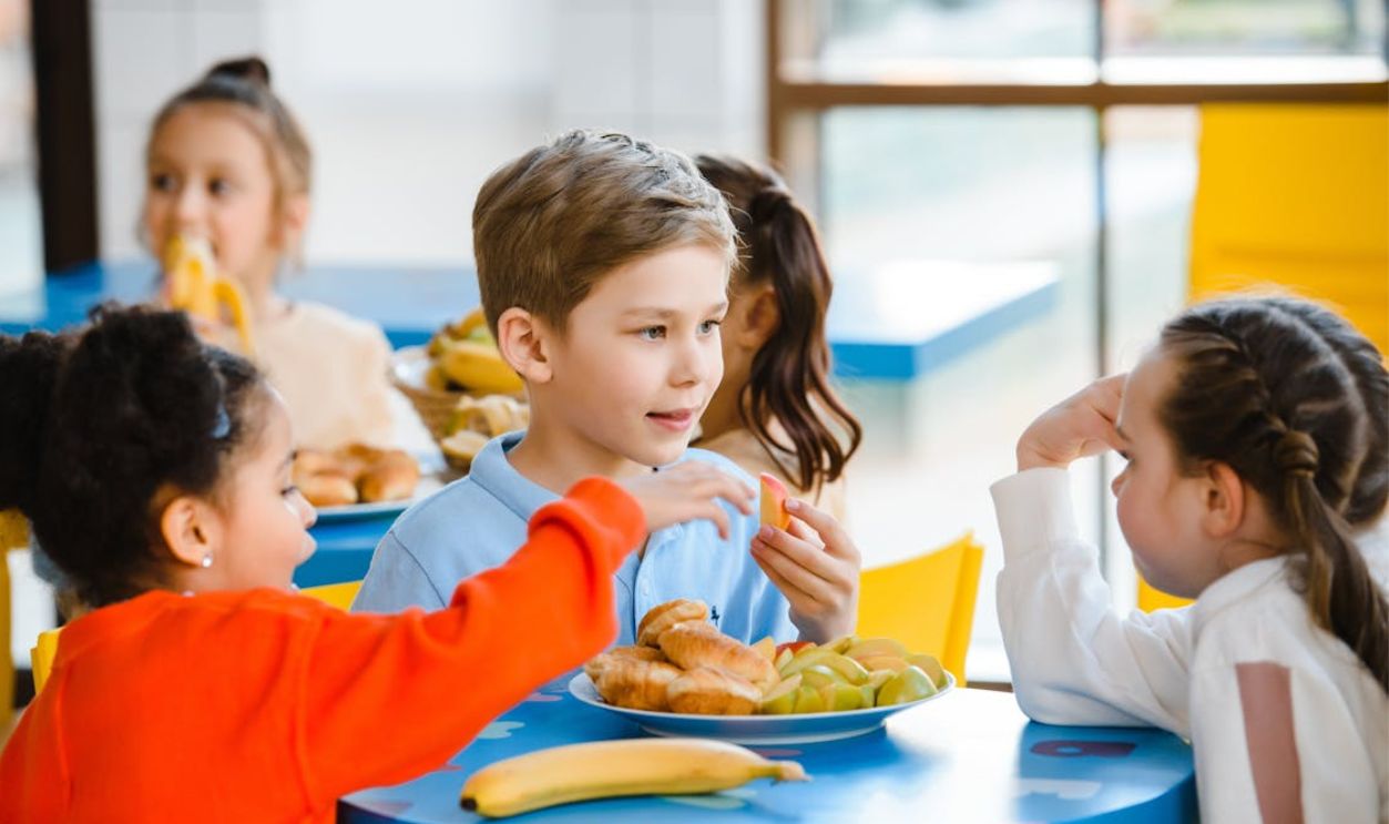 Group of diverse children enjoying a meal together indoors, fostering friendship and sharing.