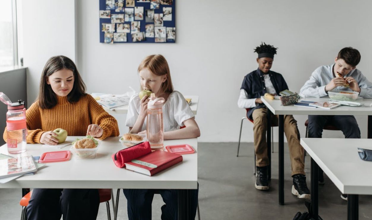 Group of teenagers enjoying lunch together in a bright classroom.