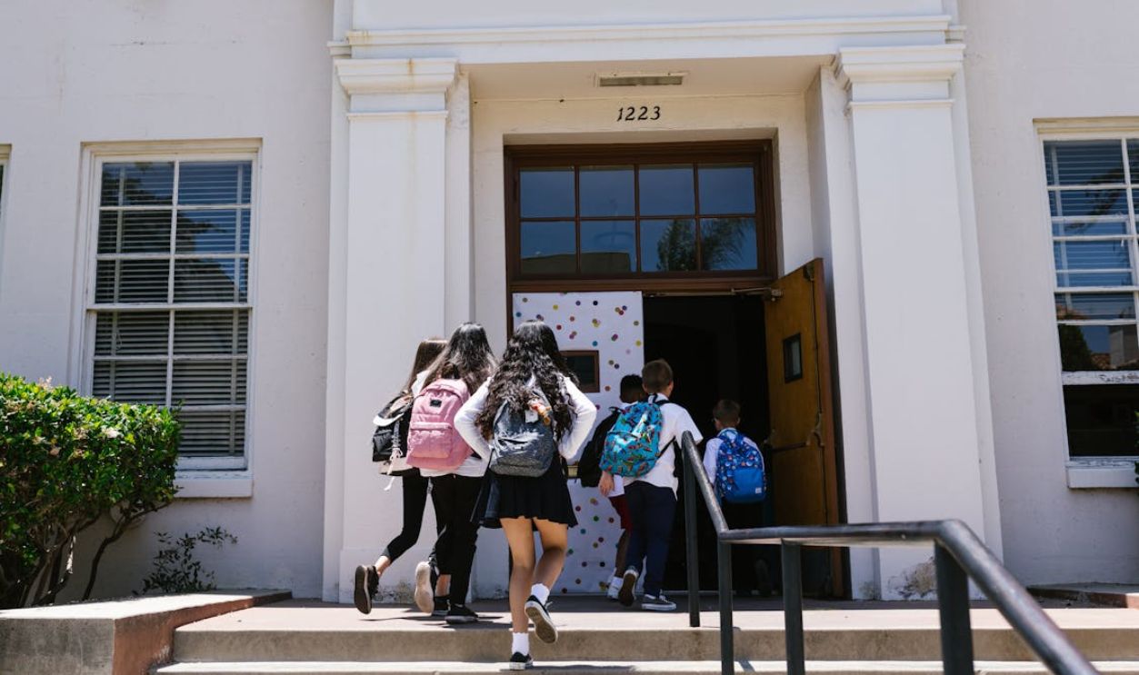 Group of students with backpacks entering a school building. Perfect for back-to-school themes.
