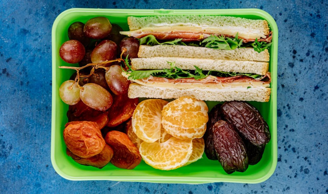 A nutritious lunch box featuring sandwiches, fresh fruit, and dried snacks, perfect for a balanced meal.