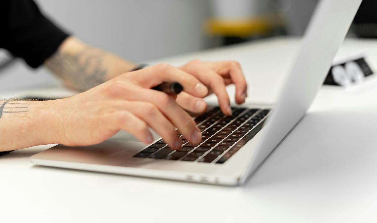Close-up of tattooed hands typing on a laptop keyboard, showcasing productivity.