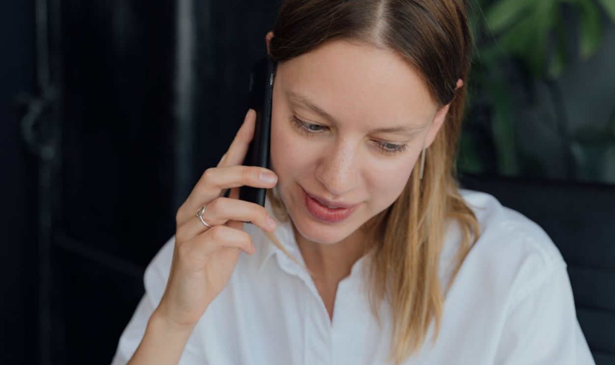 A professional woman in a white shirt making a phone call in an indoor setting, showing communication and business engagement.