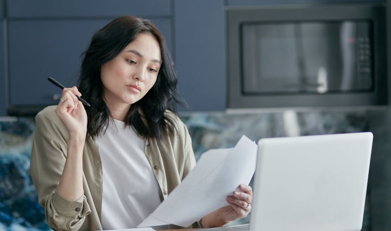 Young woman reviewing documents and working on a laptop in a modern home office setting.