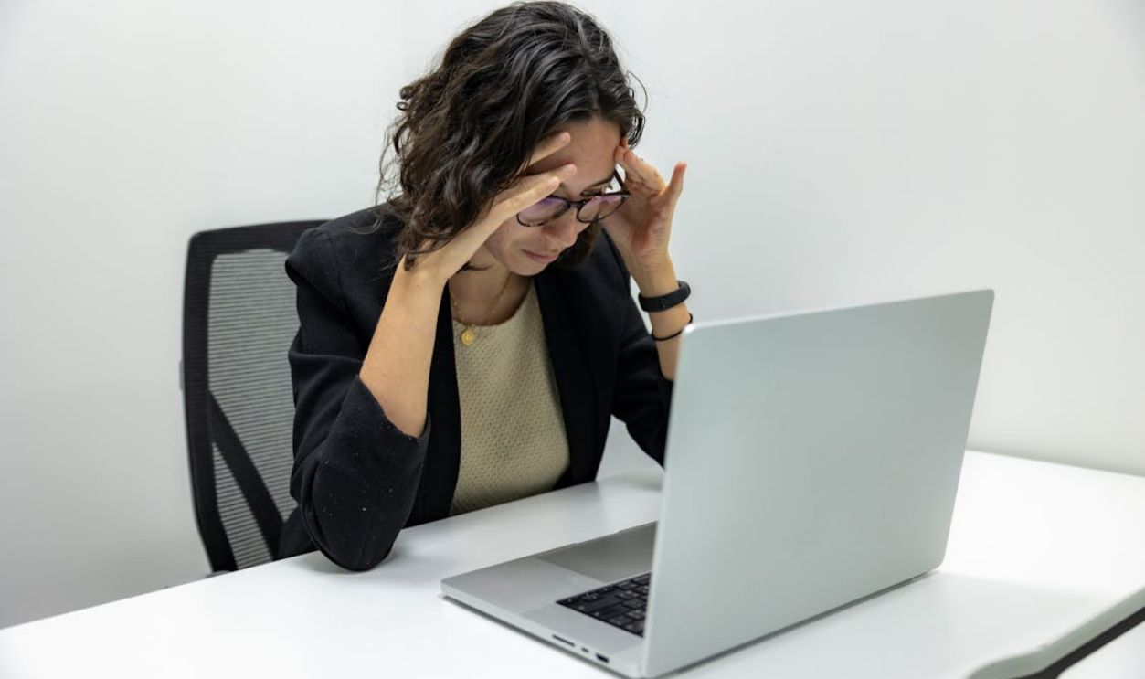 A young woman experiencing stress and fatigue while working on her laptop in an office setting.