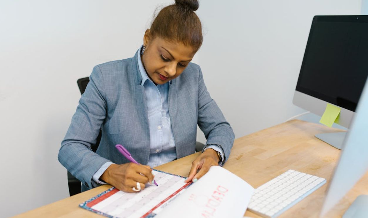 Businesswoman writing plans in a calendar at her office desk.