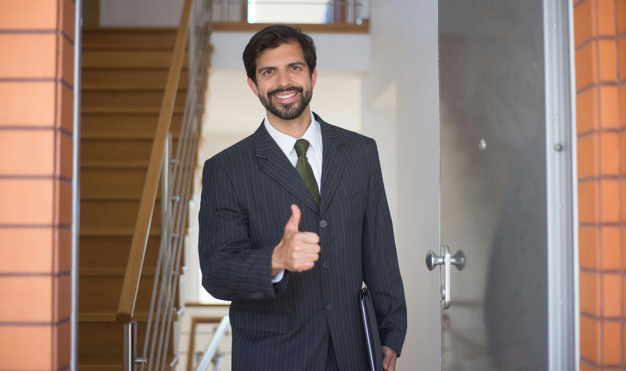 Smiling realtor gives a thumbs up at a modern open house.