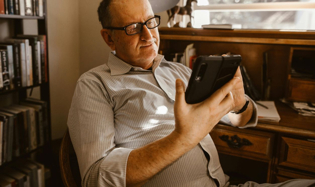Elderly man using a tablet indoors surrounded by books, showcasing technology engagement