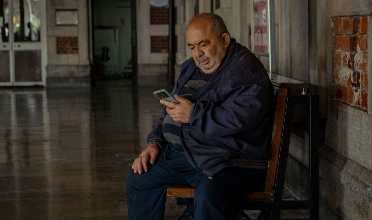 Adult man sitting on bench indoors, using smartphone for communication