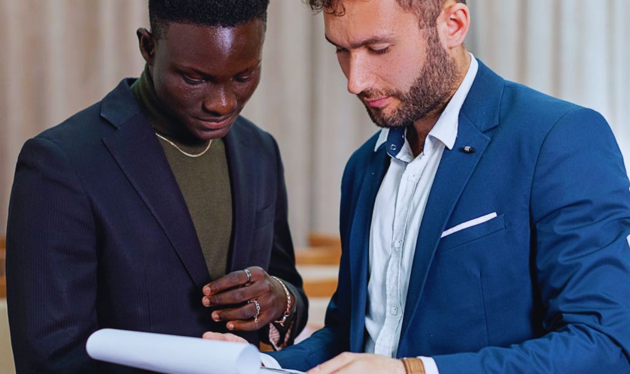 Two businessmen in suits review a contract indoors, focusing on the document