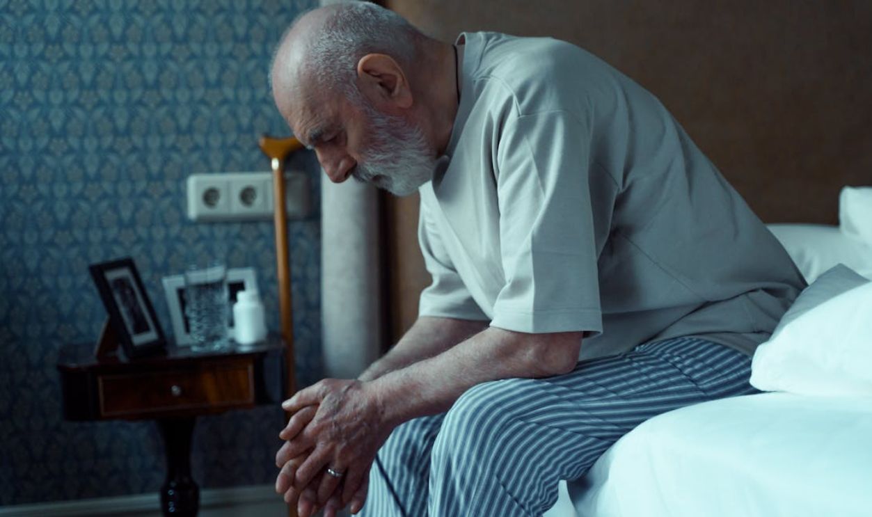 An elderly man sits thoughtfully on a bed, conveying solitude and reflection