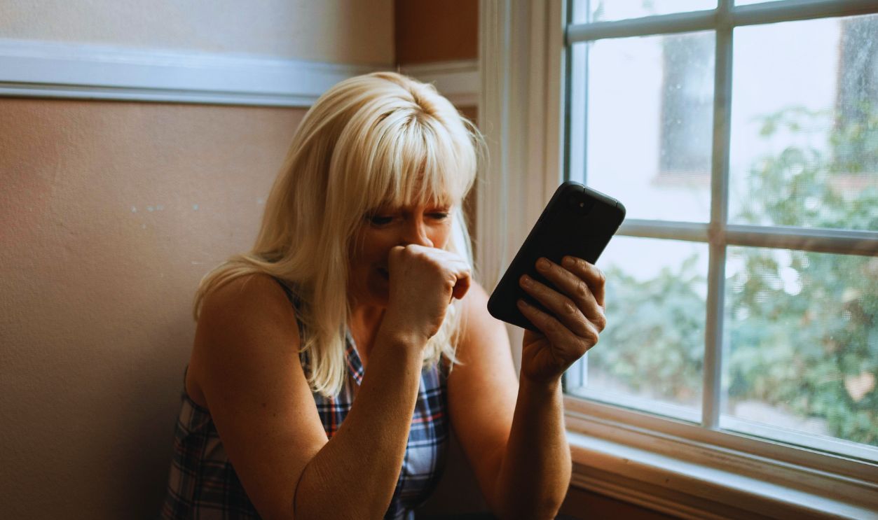 Woman sitting in deep thought by a window, holding a smartphone