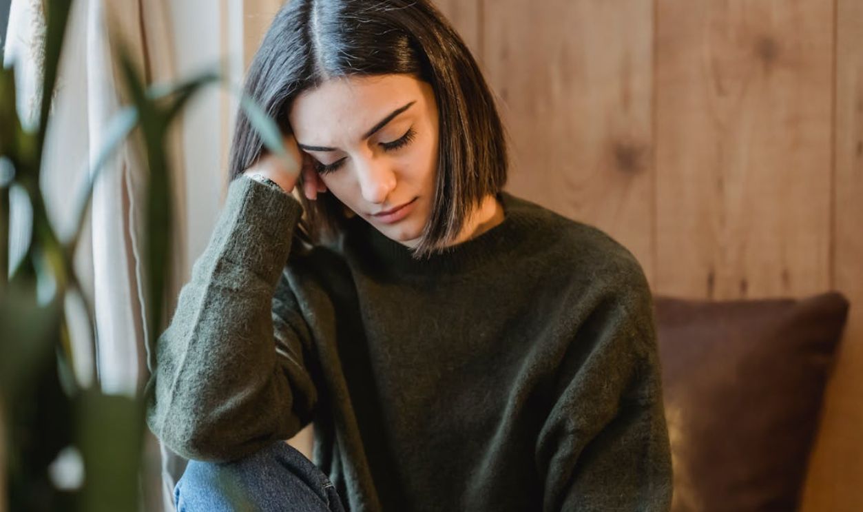 A young woman sitting indoors, leaning on her hand, looking peaceful and serene