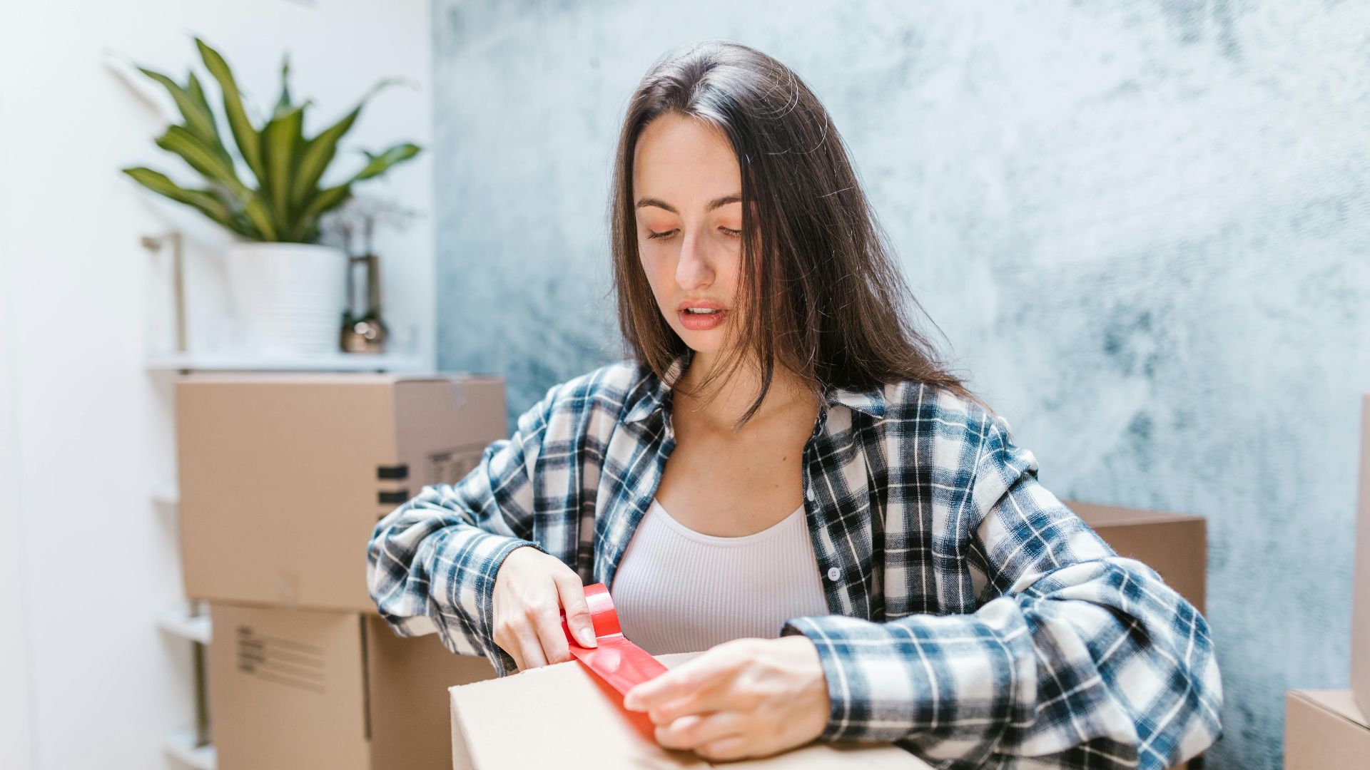 Woman sealing boxes with tape for relocation in a cozy indoor setting.