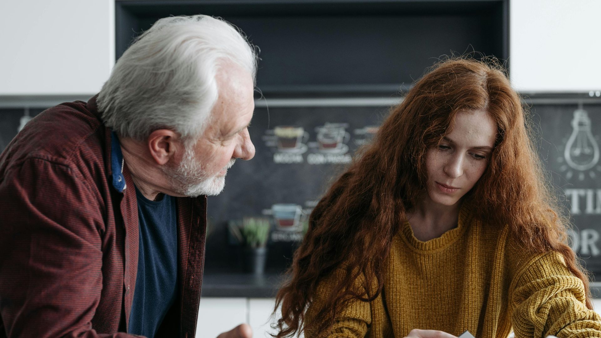Elderly man and young woman looking at a photo album together, evoking emotions and memories.