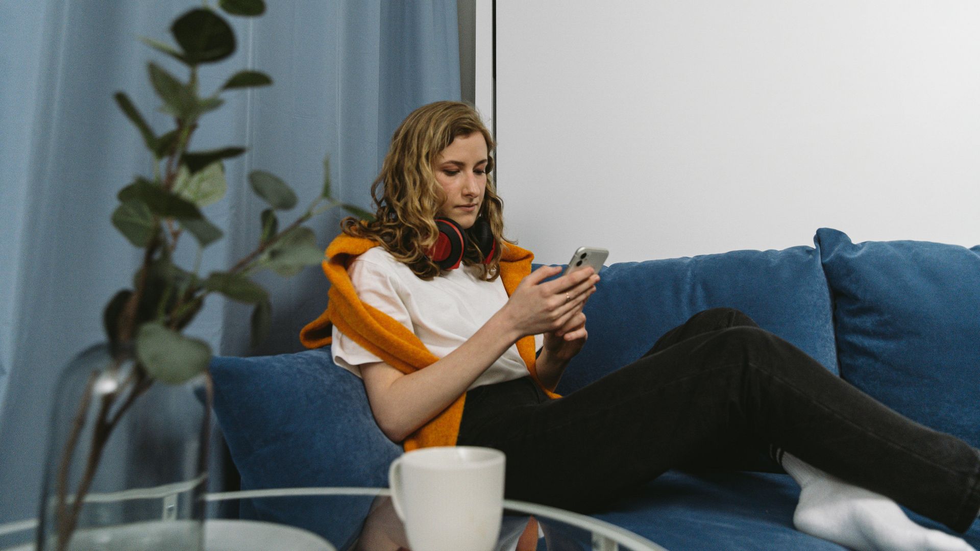 A woman sitting on a blue sofa using a smartphone, with a modern home setting.