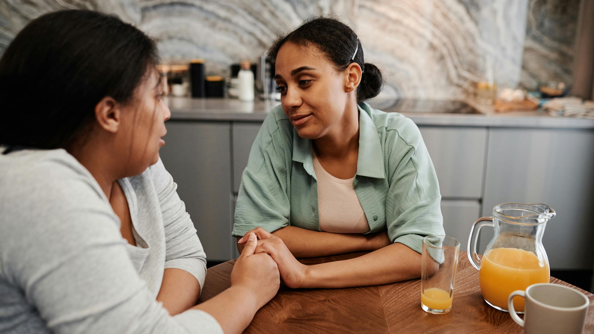 Two women engage in a supportive conversation over breakfast in a cozy kitchen setting.