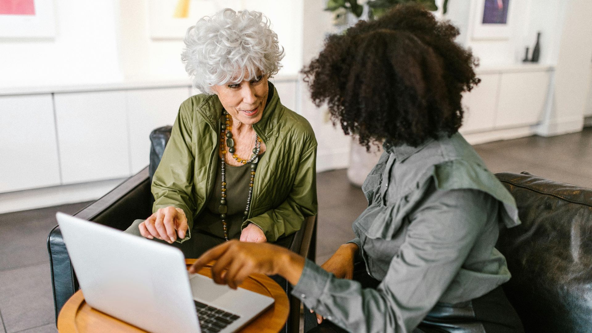 Two women discussing work on a laptop in a modern office setting.
