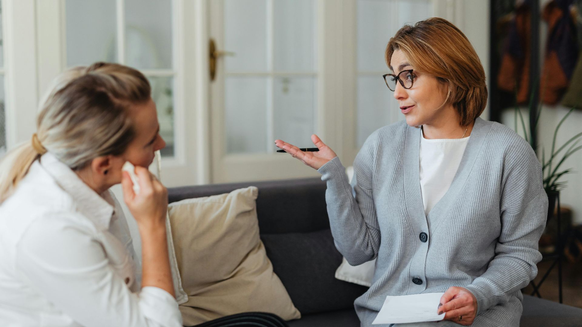 A counseling session with two women sitting on a sofa, engaged in conversation, indoors.