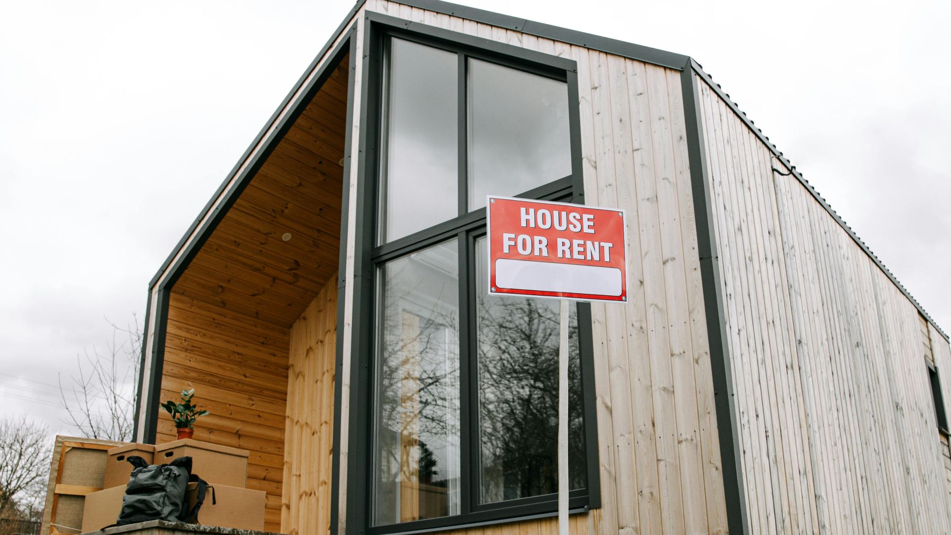 Low-angle view of a modern wooden house with a 'House for Rent' sign, showcasing contemporary architecture.