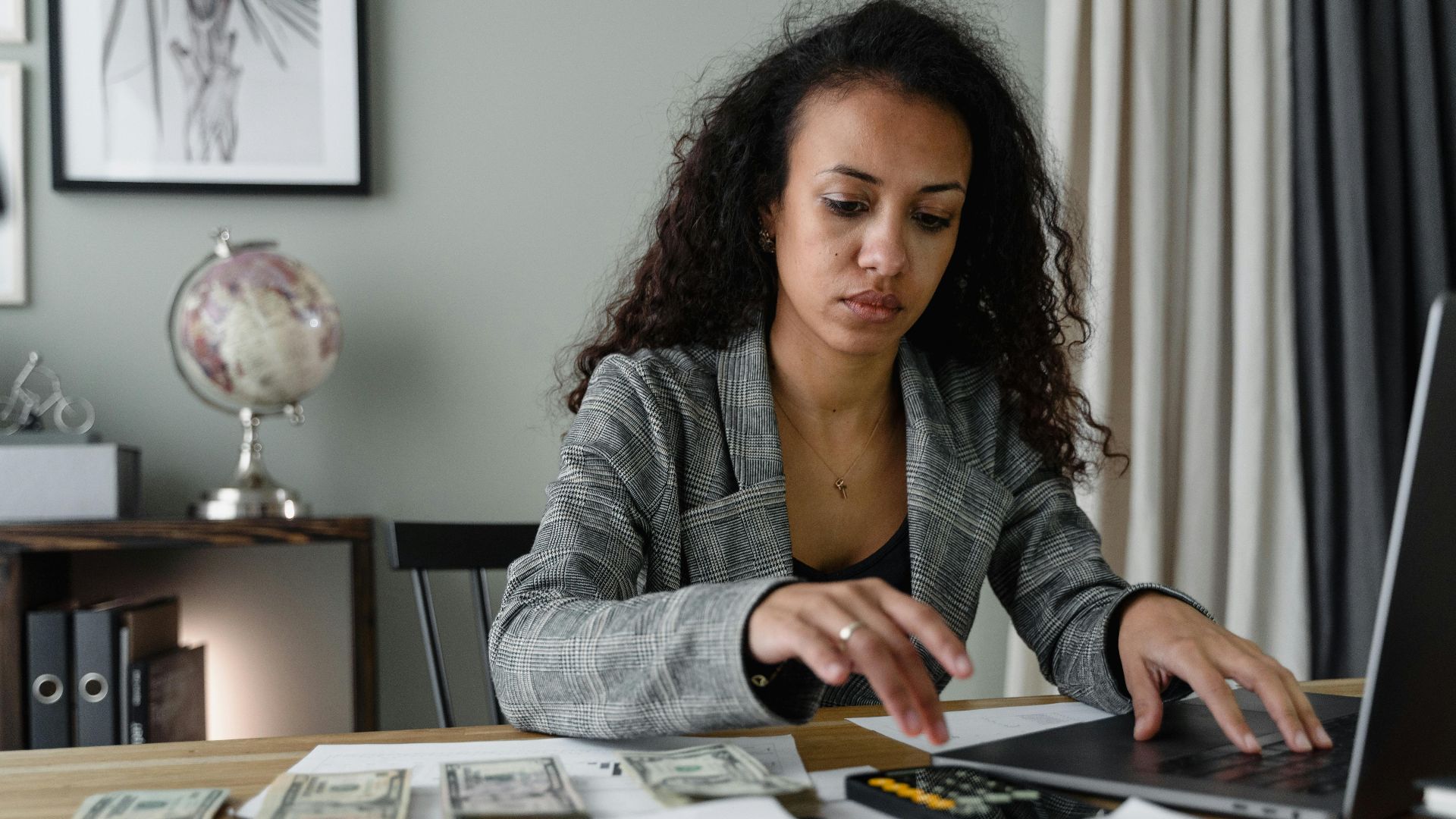 Professional woman analyzing financial documents and counting cash at office desk.